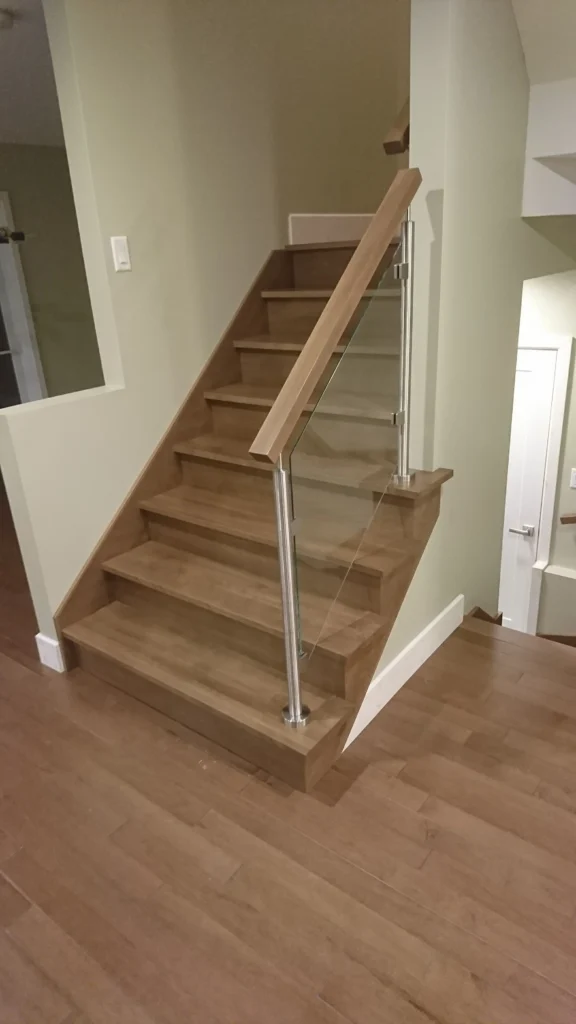 Escalier tournant en bois franc à garde-corps de verre et poteaux métalliques