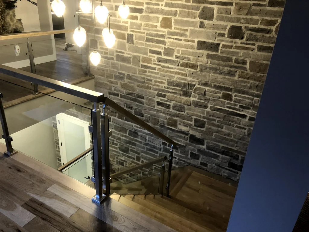 Escalier tournant de bois gris-brun à garde-corps de verre et poteaux de bois à Carignan (vue 2)