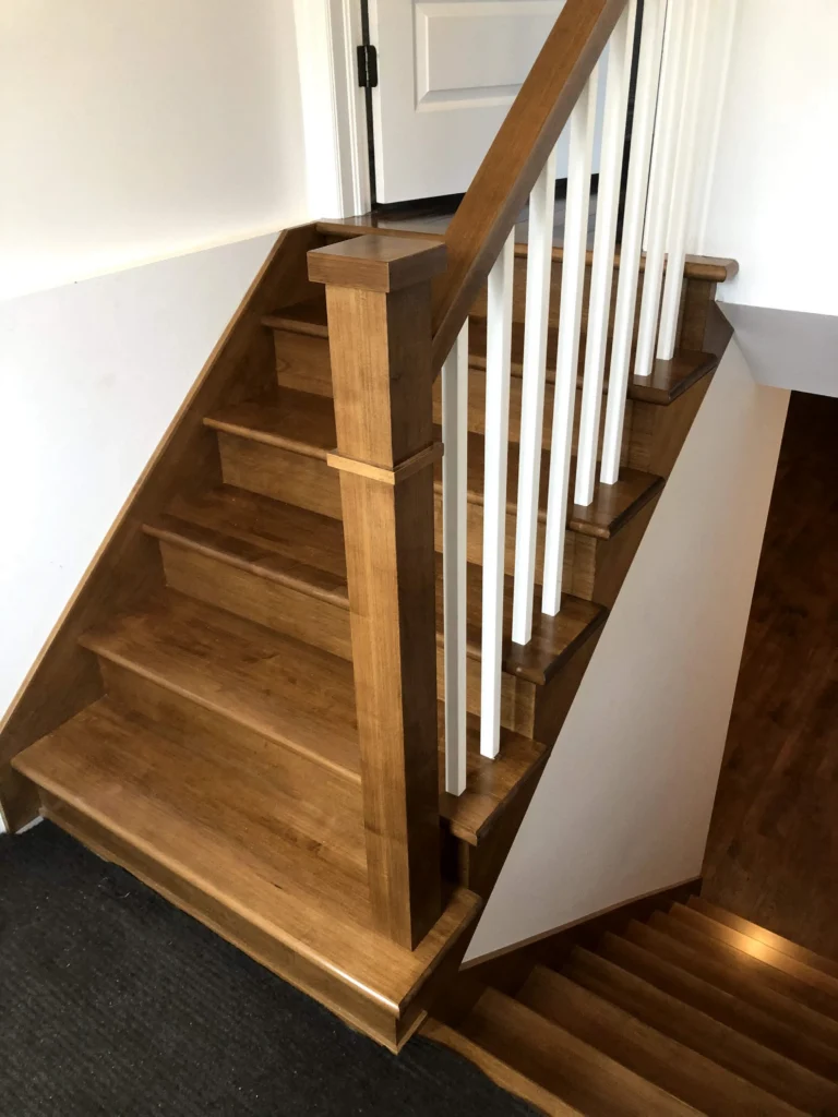Escalier tournant de bois miel à barreaux blancs et main courante de bois