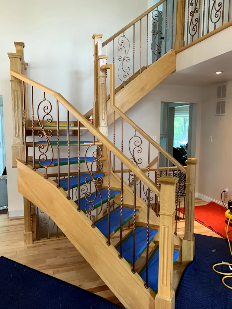 Escalier tournant de bois clair à barreaux de fer forgé ornementaux