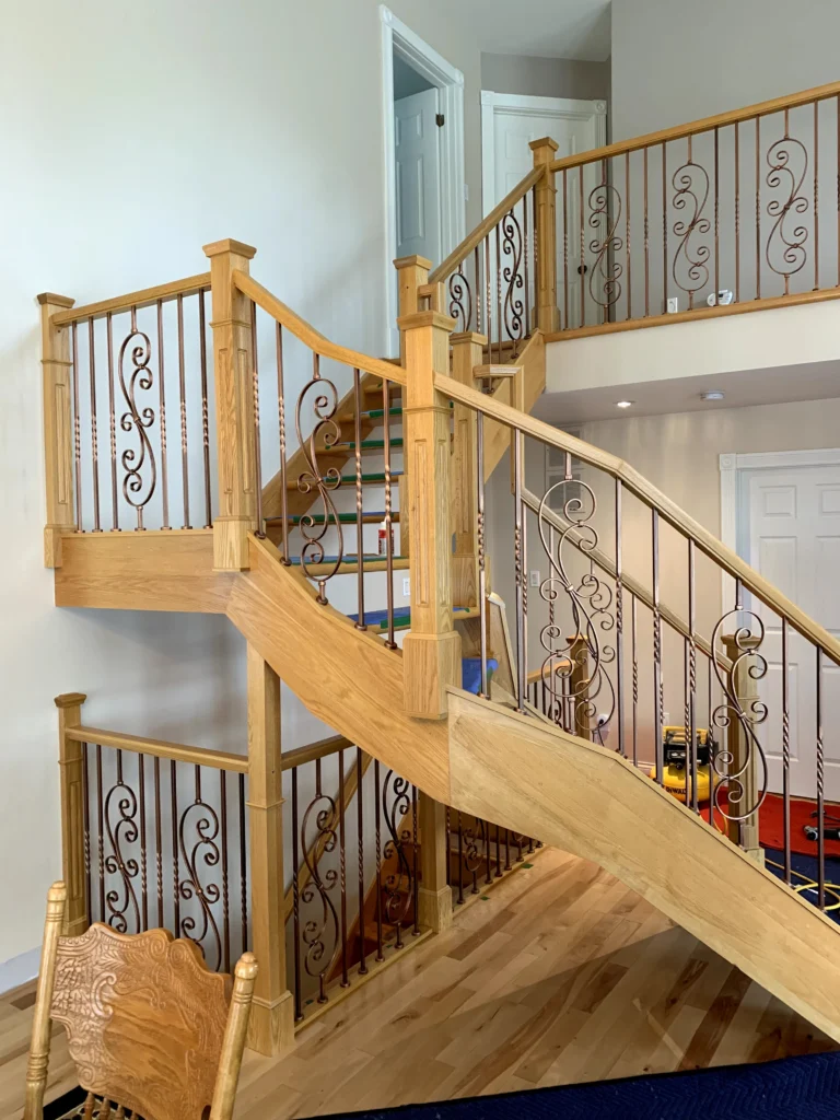 Escalier tournant de bois clair à barreaux de fer forgé ornementaux à Saint-Hubert (vue 2)