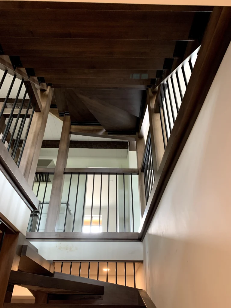 Cage d'escalier sur plusieurs niveaux en bois foncé avec garde-corps à barreaux métalliques noirs