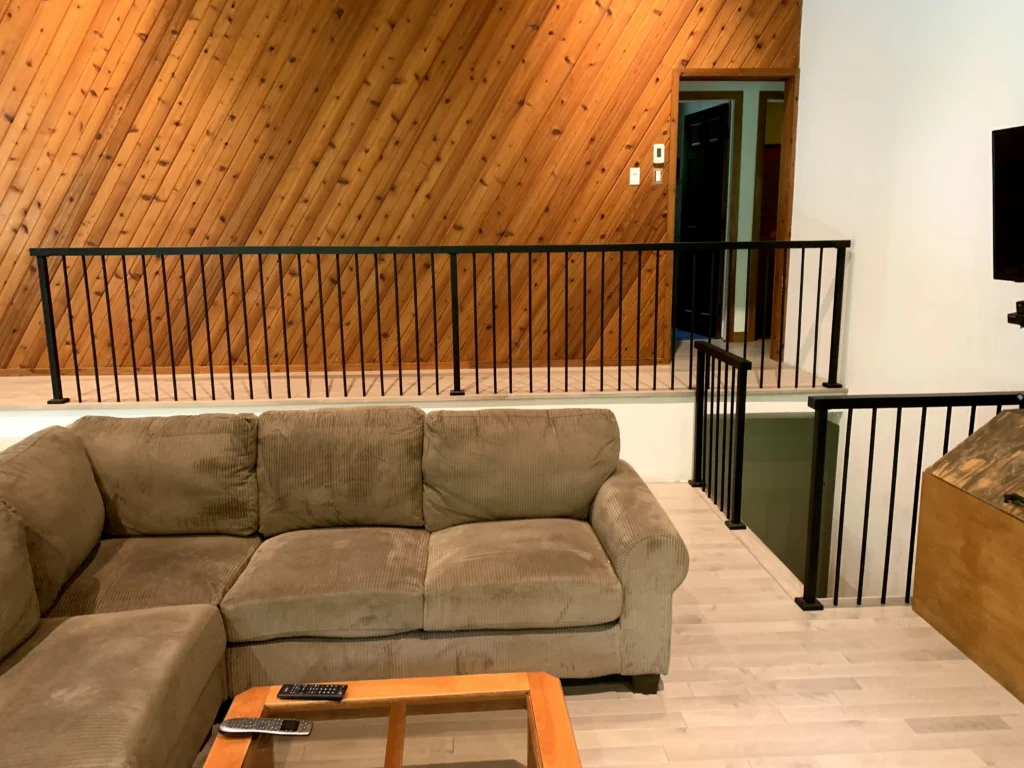 Séjour de chalet aux murs de pin avec garde-corps de métal noir autour de la trémie