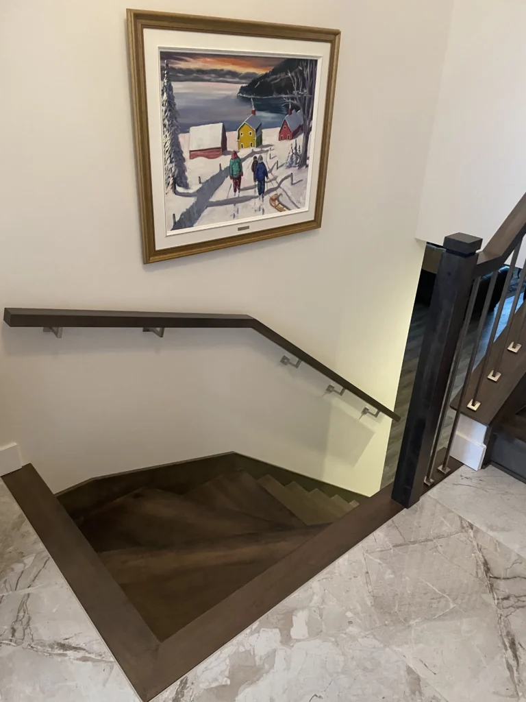 Trémie d'escalier en bois foncé avec main courante murale et garde-corps à barreaux métalliques