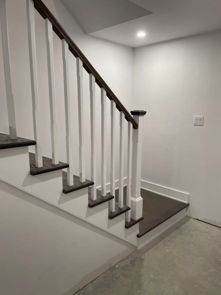 Escalier en bois gris et blanc avec poteau et barreaux de bois blancs dans un sous-sol