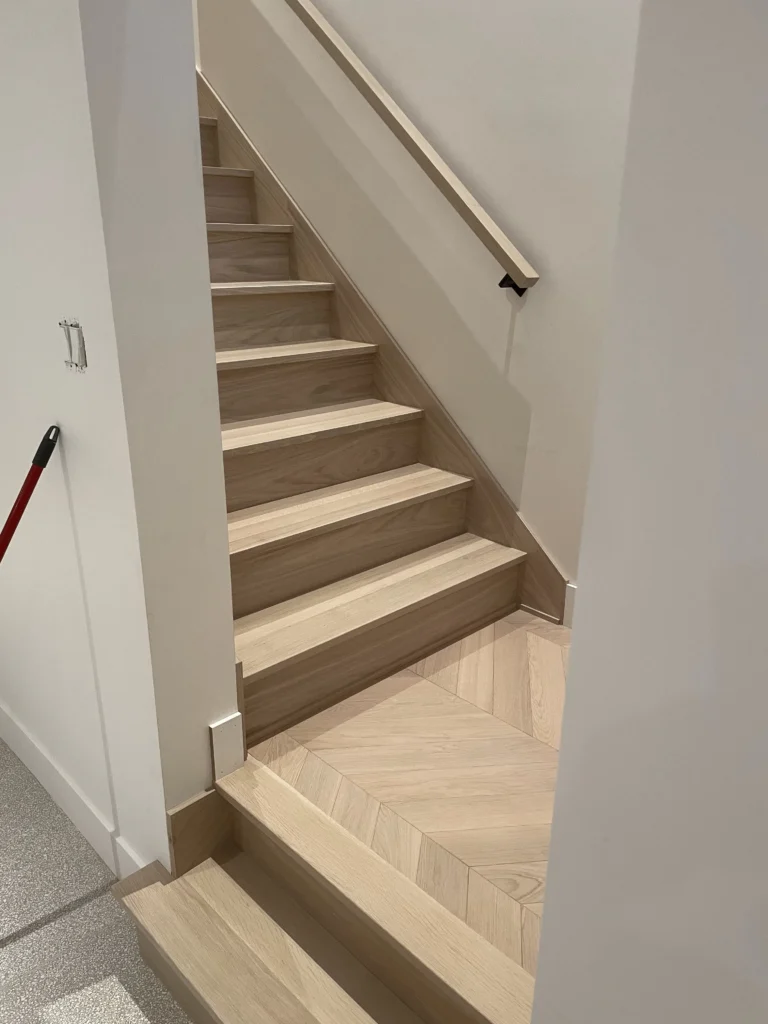 Volée d'escalier en chêne blanc et main courante murale carrée, palier à chevrons en contrebas