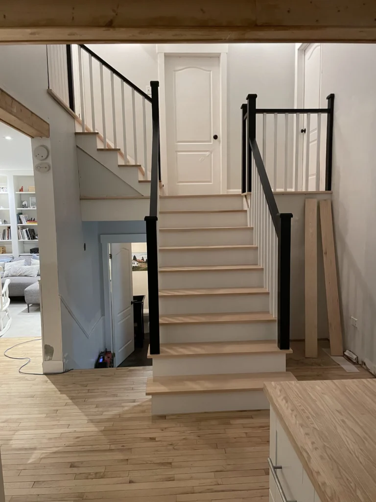 Volées d'escalier en érable et blanc avec poteaux et main courante noirs sous une poutre de pin
