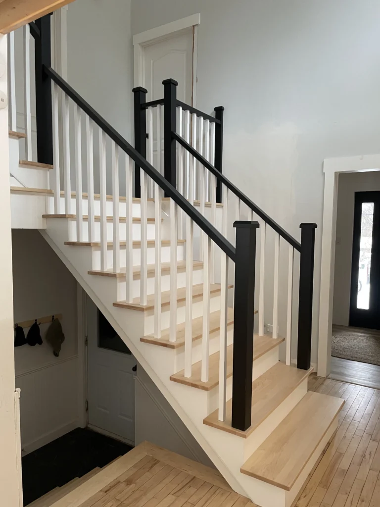 Escalier d'érable à poteaux noirs et barreaux blancs dans une entrée rénovée