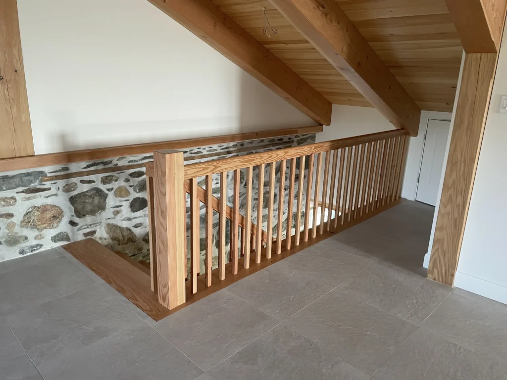 Mezzanine à barreaux de bois clair devant un mur de pierre, à Varennes