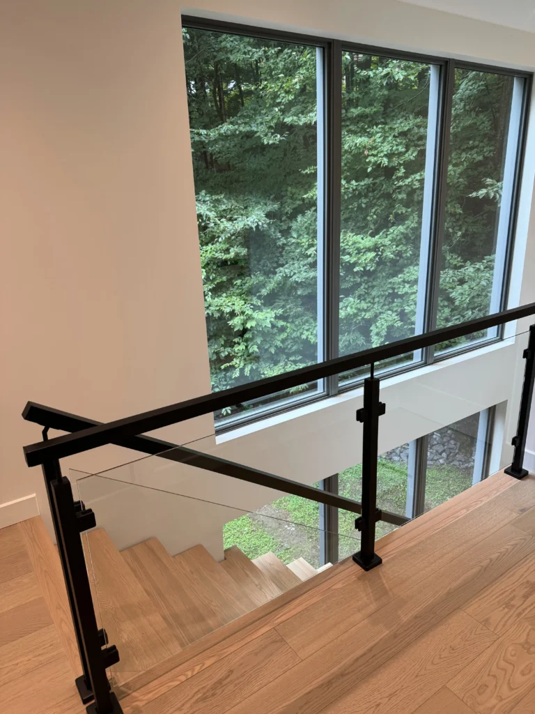 Palier de l'escalier devant une grande fenêtre sur la forêt
