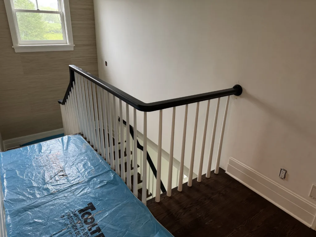 Escalier tournant rénové vu du palier, marches foncées, contremarches blanches et barreaux blancs sous une main courante noire