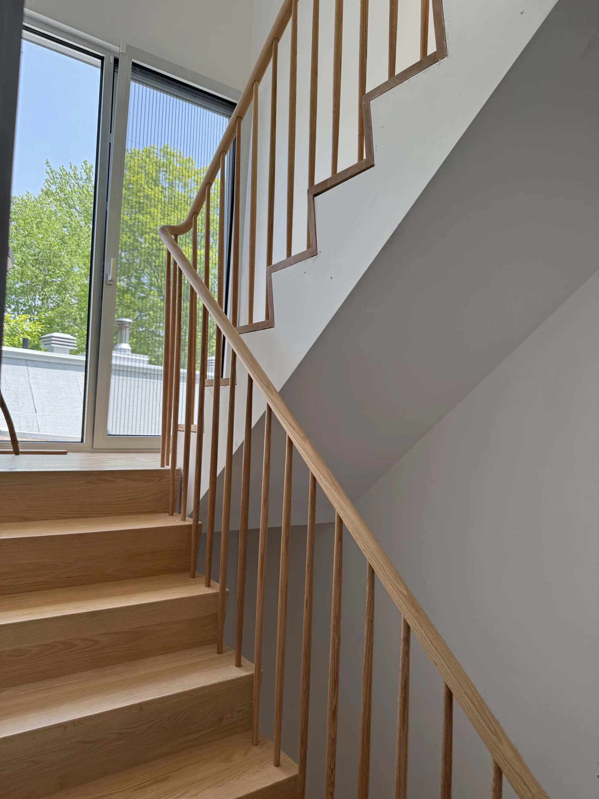 Escalier tournant en frêne à barreaux ronds devant une verrière — vue principale