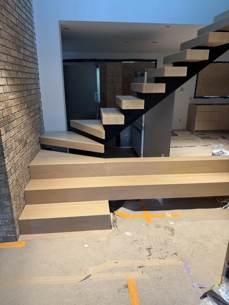 Escalier à limon central d'acier noir avec marches flottantes de chêne blanc et marches rayonnantes au départ, devant un mur de brique, en fin de chantier