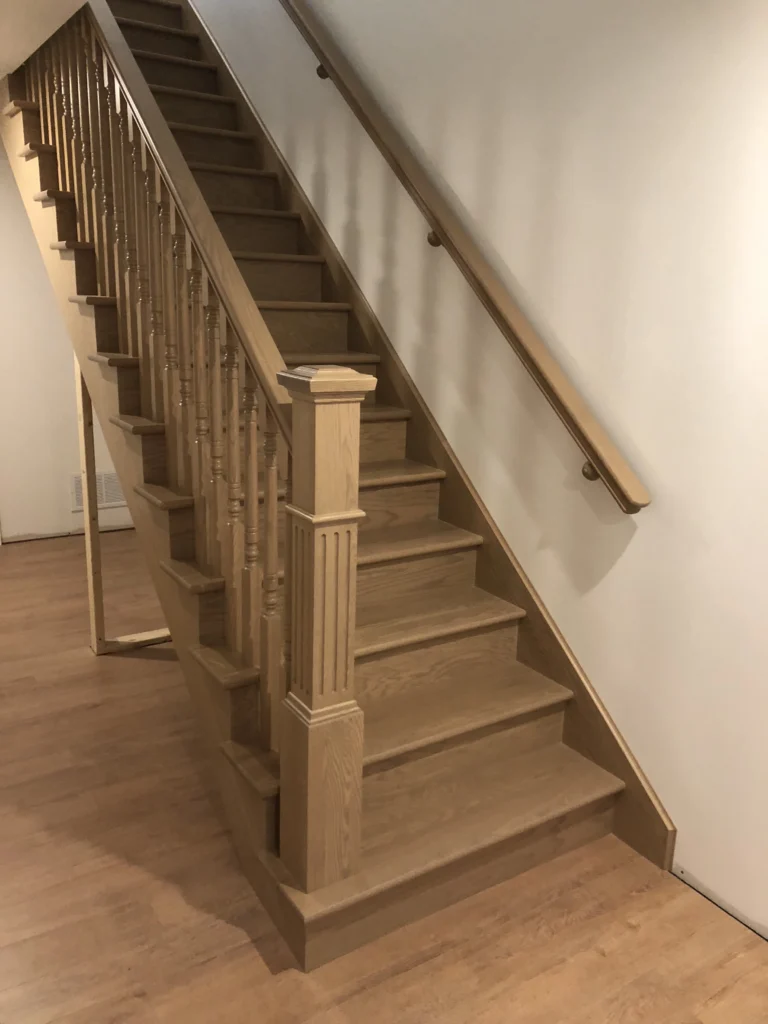 Escalier tournant en chêne naturel clair avec barreaux de bois tournés, poteau cannelé et marches de départ tournantes