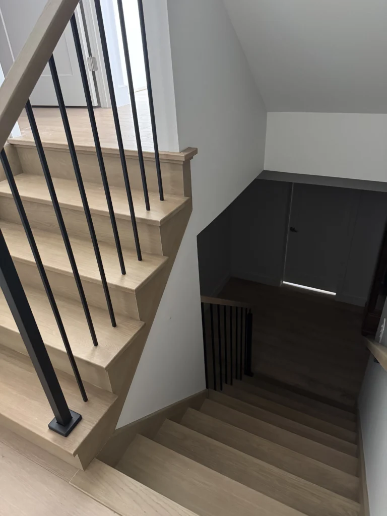 Escalier tournant en chêne pâle avec barreaux noirs et claustra de tasseaux