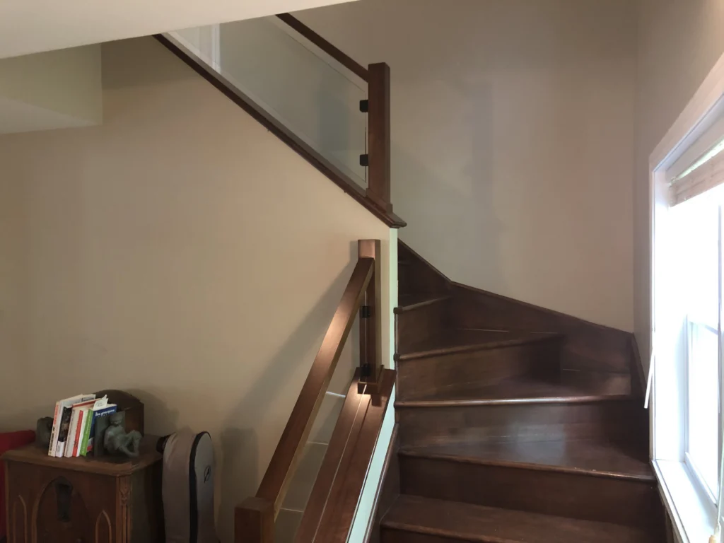 Escalier tournant en bois teinté brun foncé avec garde-corps de verre