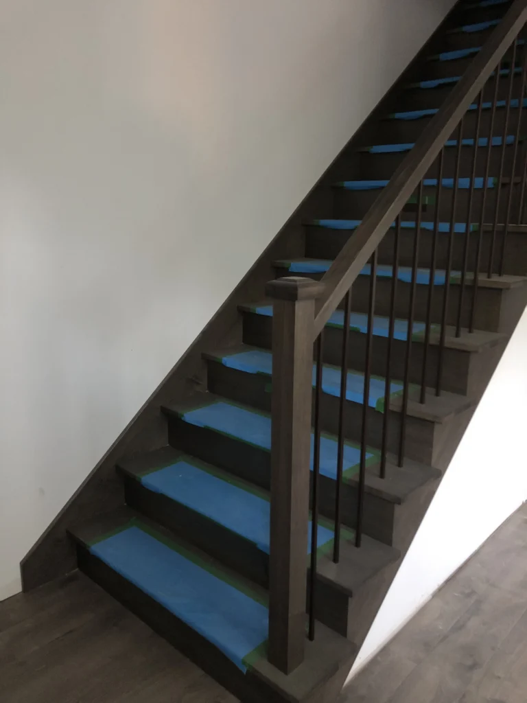 Escalier tournant en chêne teinté gris fumé avec barreaux métalliques noirs, poteau et main courante de bois