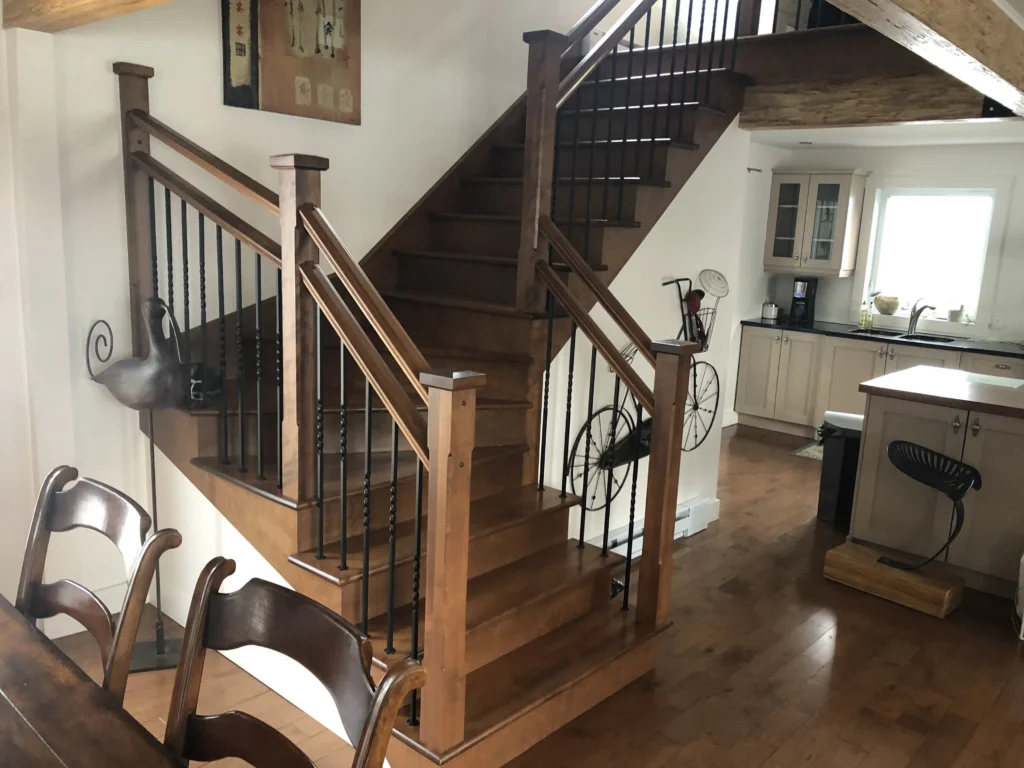 Escalier demi-tournant en érable teinté miel avec barreaux de fer forgé torsadés