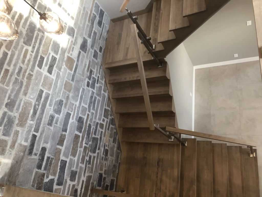 Escalier tournant à contremarches ouvertes et garde-corps de verre devant un mur de pierre