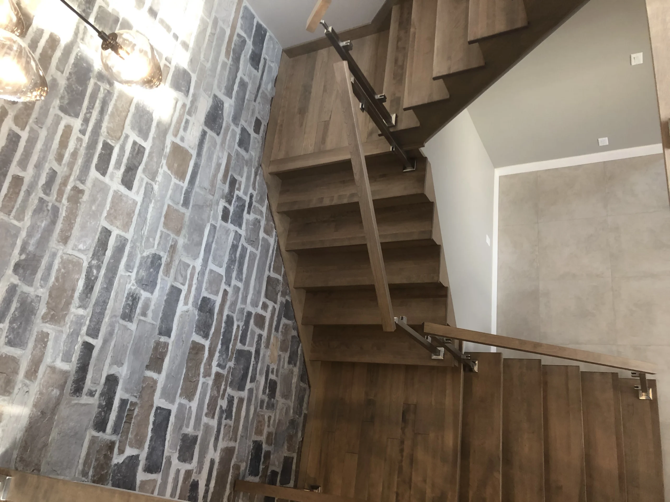 Escalier tournant à contremarches ouvertes et garde-corps de verre devant un mur de pierre — vue principale