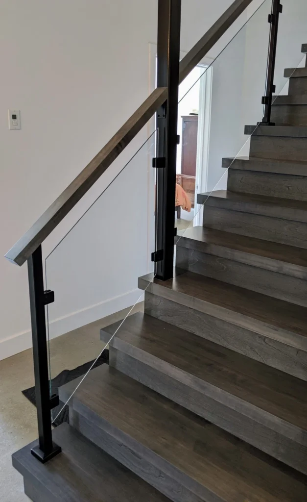 Escalier tournant en chêne teinté gris avec garde-corps de verre et poteaux noirs