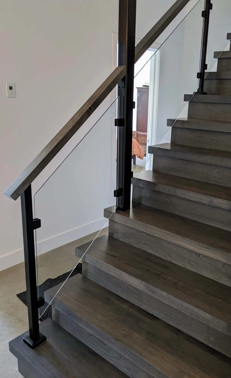 Escalier tournant en chêne teinté gris avec garde-corps de verre et poteaux noirs — vue principale