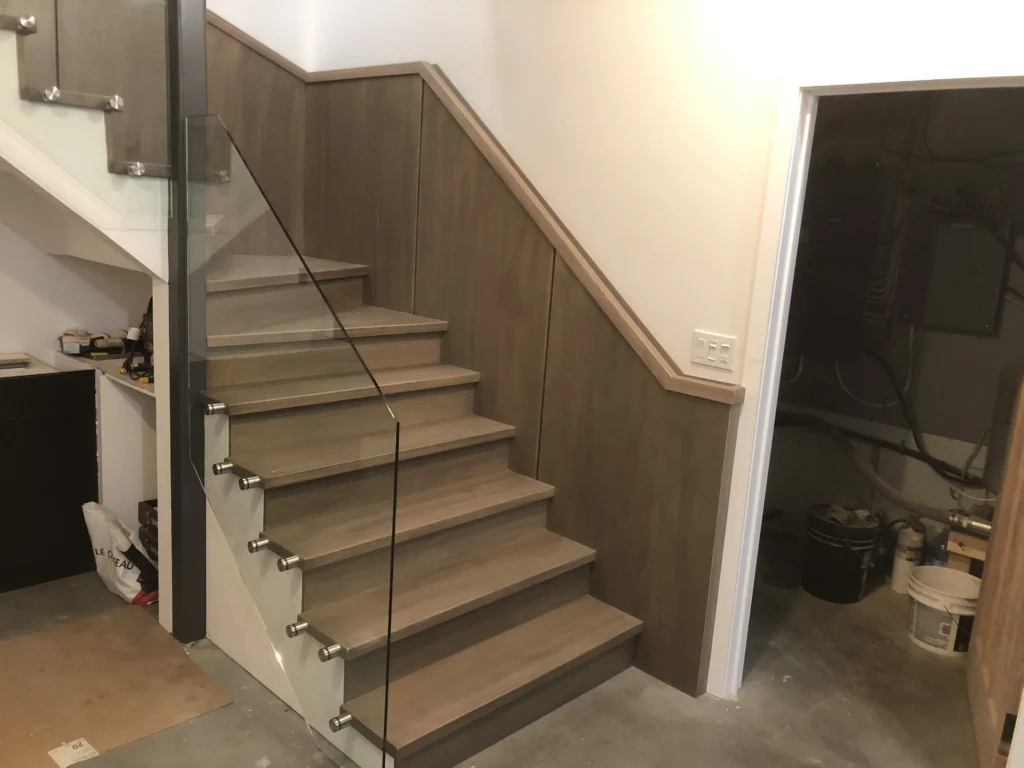 Escalier droit en érable gris-brun avec garde-corps de verre au sous-sol
