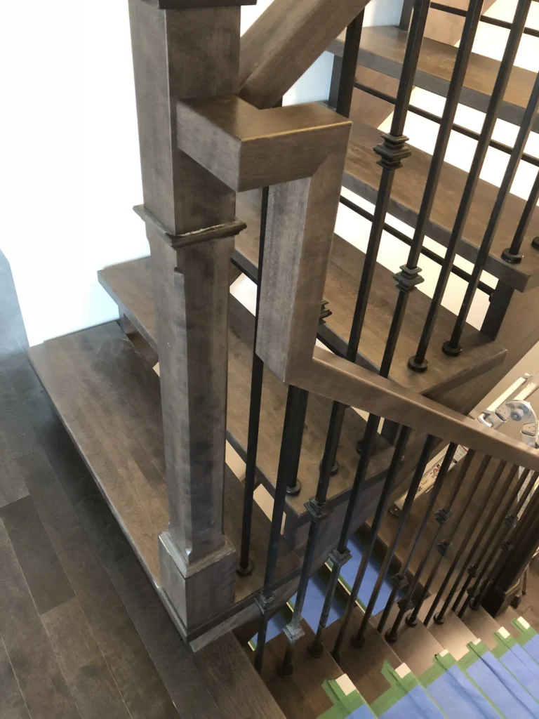 Poteau de bois gris-brun et barreaux de fer forgé d'un escalier tournant