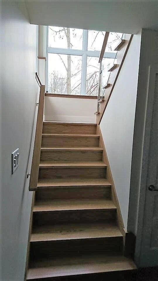 Escalier droit en chêne clair à garde-corps de verre devant une verrière