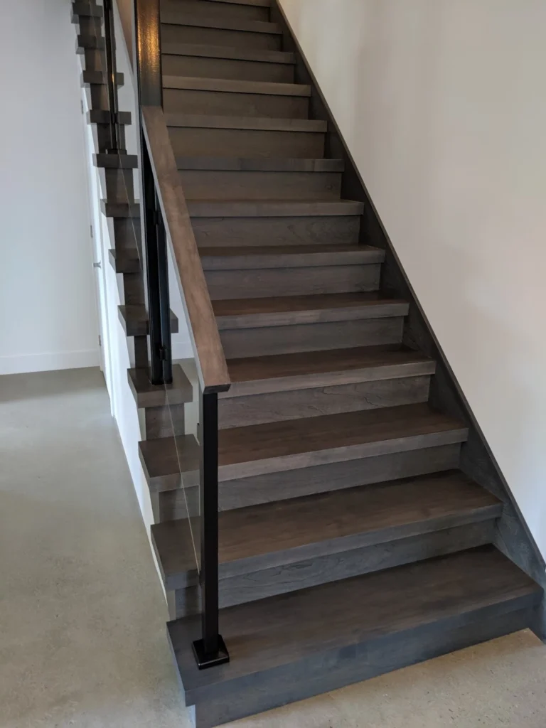 Escalier droit en bois gris-brun à garde-corps de verre et poteaux noirs