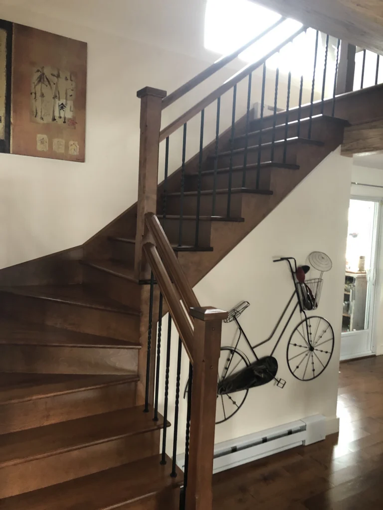 Escalier tournant en bois teinté brun à barreaux de fer forgé