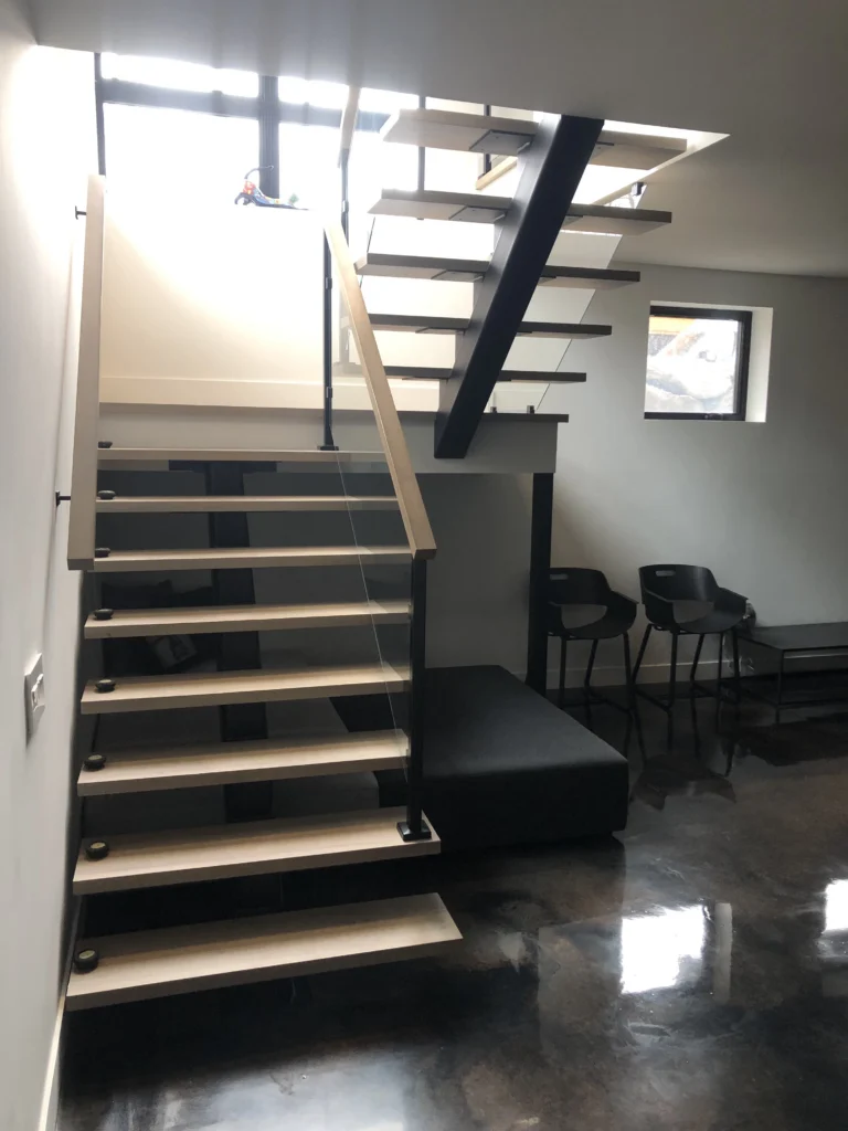 Escalier suspendu sur mesure à marches d'érable clair sur limon central d'acier noir avec garde-corps de verre, sous-sol d'une résidence de Saint-Bruno-de-Montarville
