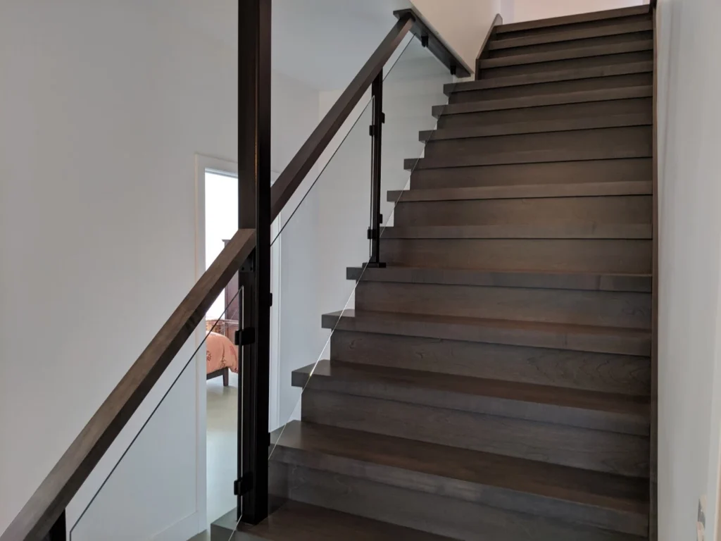 Escalier droit sur mesure en bois teinté gris-brun avec garde-corps de verre et poteaux d'acier noir, résidence à Sainte-Julie