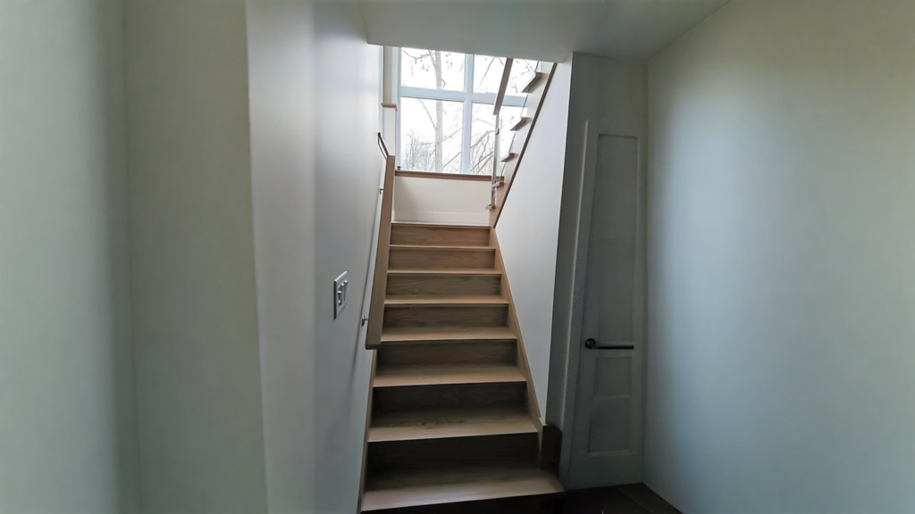 Escalier droit en chêne clair à garde-corps de verre devant une verrière