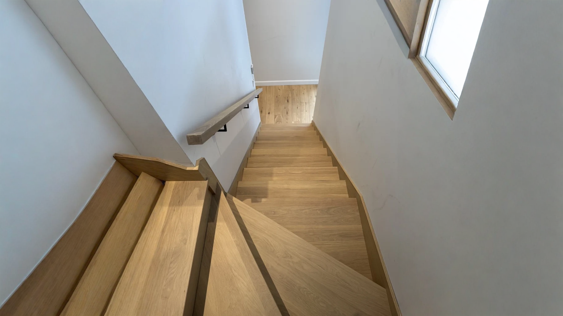 Escalier tournant en chêne blanc naturel entre deux murs avec main courante murale — vue principale