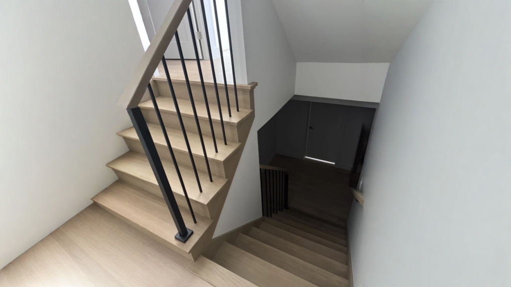 Escalier tournant en chêne pâle avec barreaux noirs et claustra de tasseaux