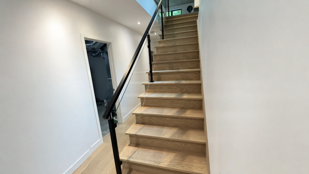 Straight staircase in blond oak with a glass railing and black metal