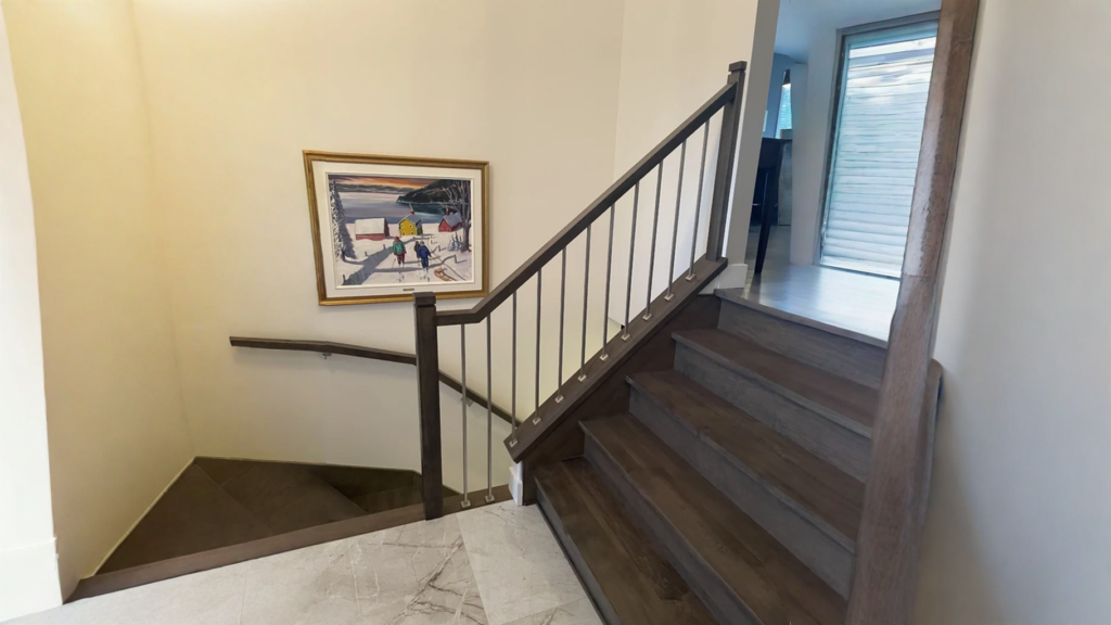 Escalier tournant en bois teinté foncé à barreaux métalliques dans un hall