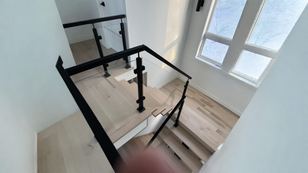 Escalier tournant à garde-corps de verre et poteaux métalliques noirs