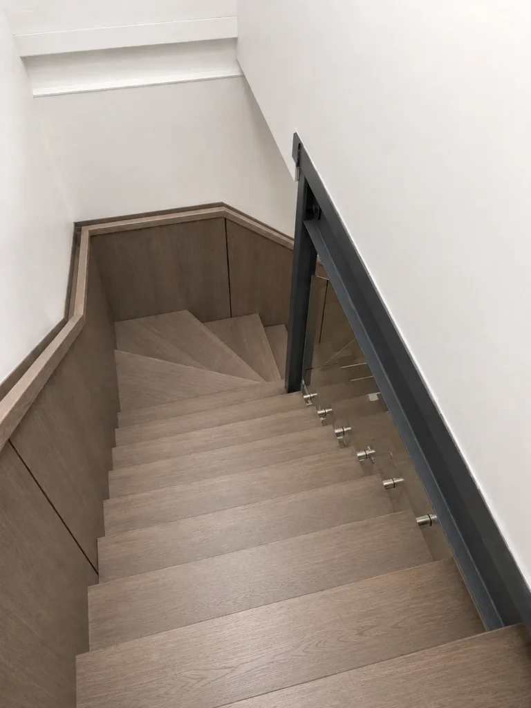 Escalier tournant en bois gris-brun à garde-corps de verre et boiserie murale